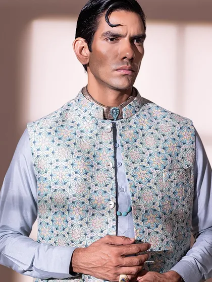 A close up on a pastel blue embroidered bandi jacket layered over a silk kurta. The addition of turquoise jewelry adds a pop of color and a touch of personal style.