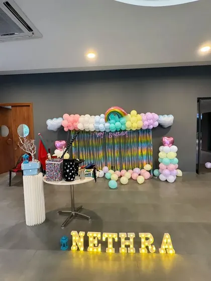 A rainbow-themed 6th birthday party for Nethra. This setup features a pastel rainbow balloon garland, a shimmery backdrop, and marquee letters, creating a bright and cheerful atmosphere.