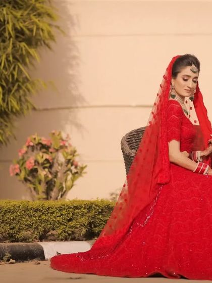A full length shot of the bride seated, her red lehenga spread out beautifully. This pose creates a regal and elegant portrait.