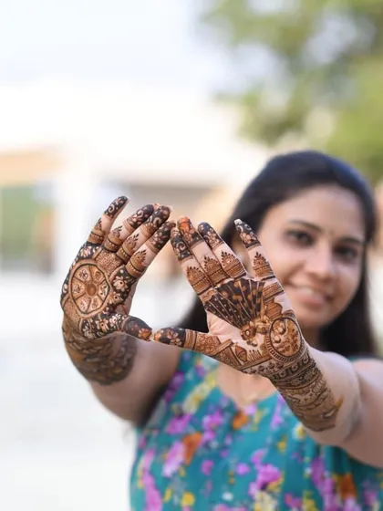 A creative pose highlighting the intricate details of the mehndi. One hand features a chakra design, while the other has a beautiful peacock.