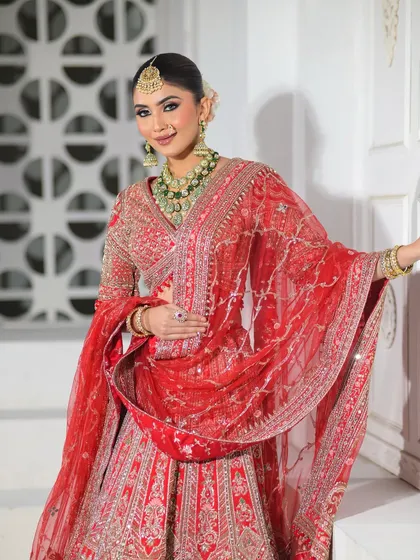 A full-body shot of the bride in a stunning red lehenga, smiling brightly. The makeup is bold enough to stand out yet elegant enough to feel timeless.