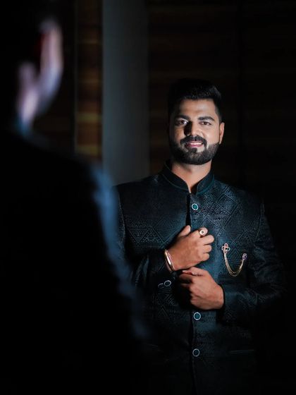 A groom looking in the mirror, ready for his engagement. The dark, patterned bandhgala jacket is a sophisticated choice.