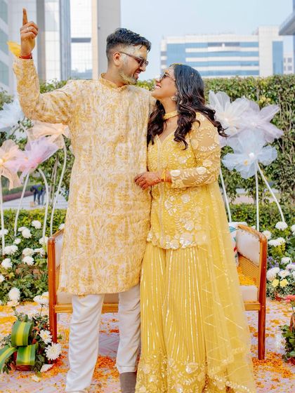 A sweet, candid moment between the couple at their Haldi, surrounded by a field of white flowers and whimsical pastel fabric blooms.