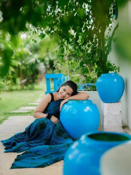 A lovely solo portrait of the bride-to-be, smiling brightly. The vibrant blue pots complement her saree, creating a colorful and cheerful composition.