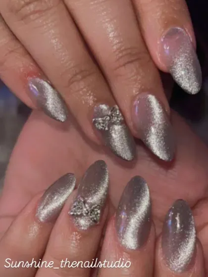 A mesmerizing silver cat eye effect on almond nails, accented with 3D rhinestone bows.
