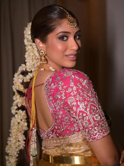 A close-up on the stunning pink blouse and the intricate floral braid. The eye makeup is defined yet soft, a perfect example of modern meets traditional South Indian bridal beauty.
