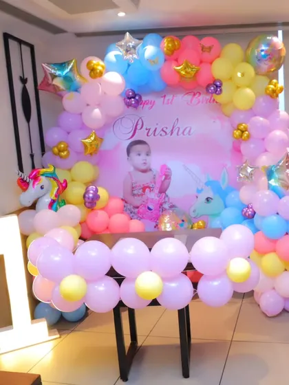 The full cake-cutting table setup for a unicorn-themed first birthday, including the backdrop, balloon decorations, and a light-up number '1'.