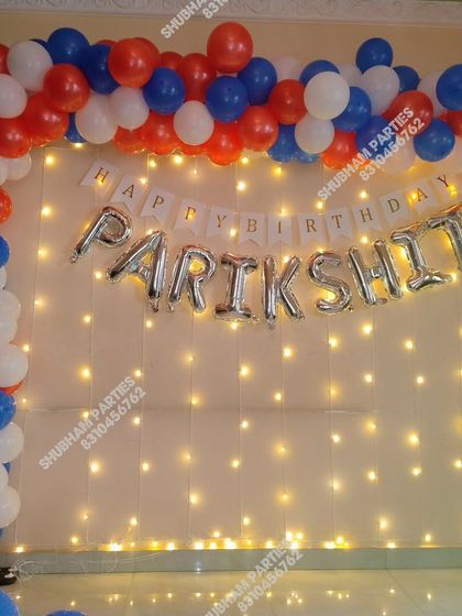 A patriotic-themed birthday decoration with red, blue, and white balloons and a fairy light wall.