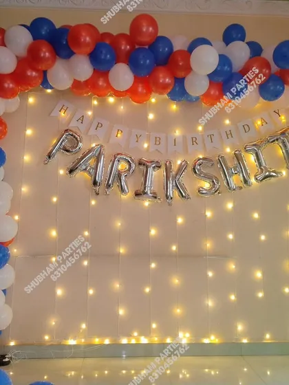 A patriotic-themed birthday decoration with red, blue, and white balloons and a fairy light wall.