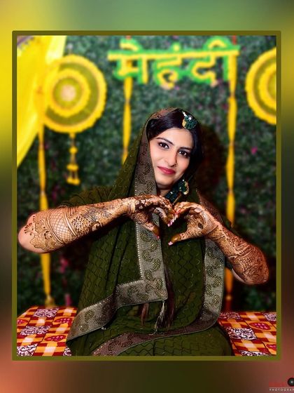 A bride making a heart shape with her hands to showcase her beautiful mehndi design, with a festive backdrop.