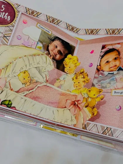 A pop-up element inside the baby album, showing the '5 months' milestone with vintage-style baby illustrations.