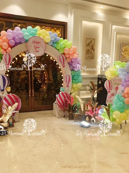 A full view of the hot air balloon themed entrance, showing the circular arch and a welcome sign area. The use of pampas grass and pastel balloons creates a soft, boho-chic vibe.