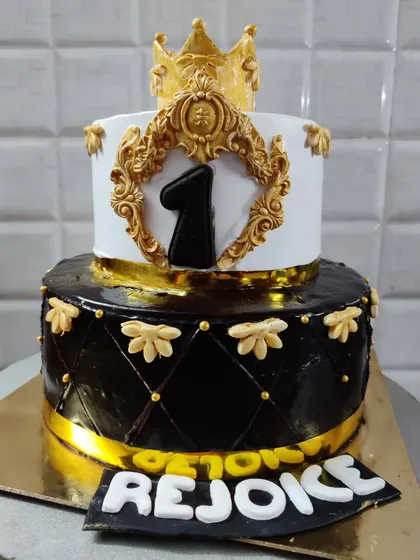 A grand two-tier cake for a royal first birthday celebration. The design features a quilted black bottom tier and an elegant white top tier, complete with a golden crown.