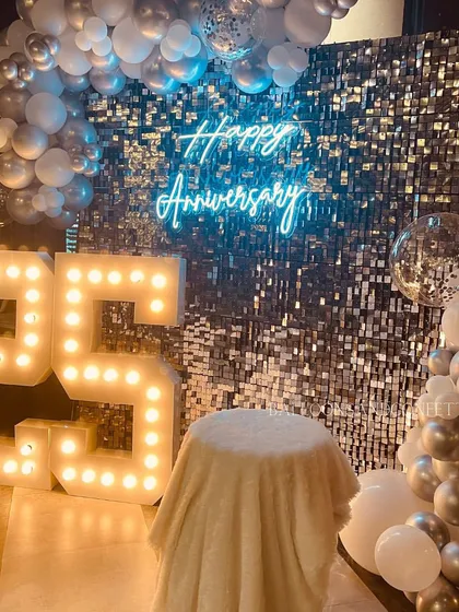 Celebrating a 25th anniversary with all the sparkle it deserves. This setup features a silver sequin wall, large marquee numbers, and a silver and white balloon arch.