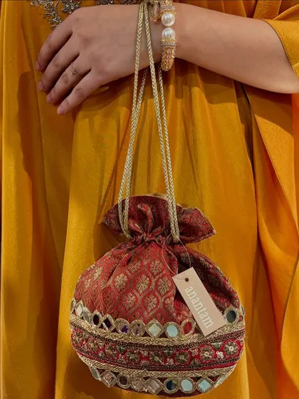 This red potli is adorned with shimmering mirror work, making it a perfect accessory for a sangeet or wedding reception.