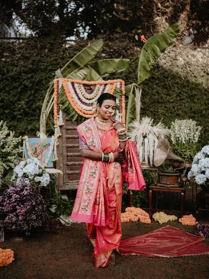 A full-length portrait of a bride in her pink nauwari saree, set against a backdrop of traditional decor. This shot captures the complete bridal look and the festive atmosphere.