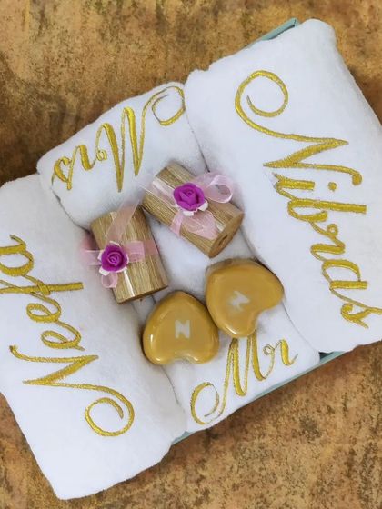 This wedding gift hamper for 'Neela' and 'Nibras' is packed with personalized goodies. It has custom name bath towels, 'Mr & Mrs' hand towels, initialed soaps, and luxury candles for a romantic touch.
