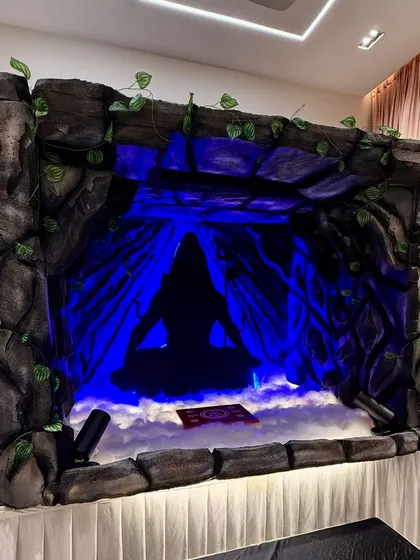 A unique cave themed Ganpati decoration for a home. The setup uses faux rock panels, dramatic blue lighting, and artificial fog to create a mystical Amarnath cave effect.