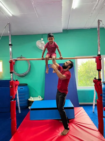 An instructor carefully spots a young child sitting on the high bar. Safety is my top priority, and my team is always there to guide and support every child as they learn new skills.
