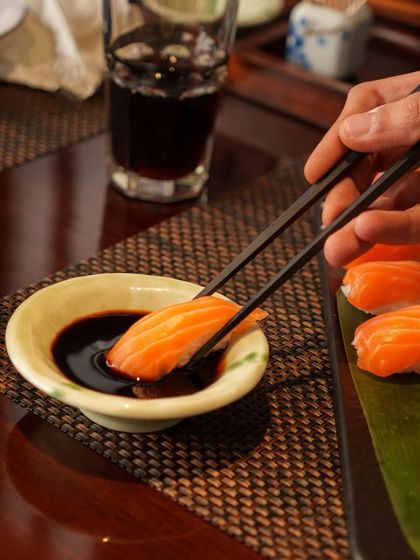 A guest enjoys a piece of Salmon Nigiri, dipping it lightly in soy sauce. This simple moment captures the essence of enjoying authentic, high-quality sushi.