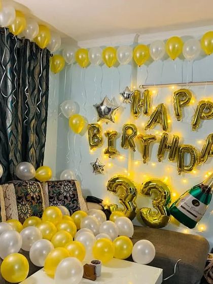 A full view of the yellow and white 33rd birthday room decoration. The couch is surrounded by balloons, and the wall features foil letters and fairy lights.