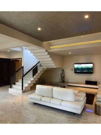 This living room combines a clean white aesthetic with interesting ceiling textures and a prominent staircase. The L-shaped sofa provides ample seating, making it a practical and stylish family space.