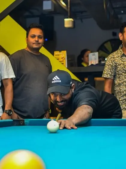 A player lines up a crucial shot at the pool table, with his friends watching intently. The focus is real.