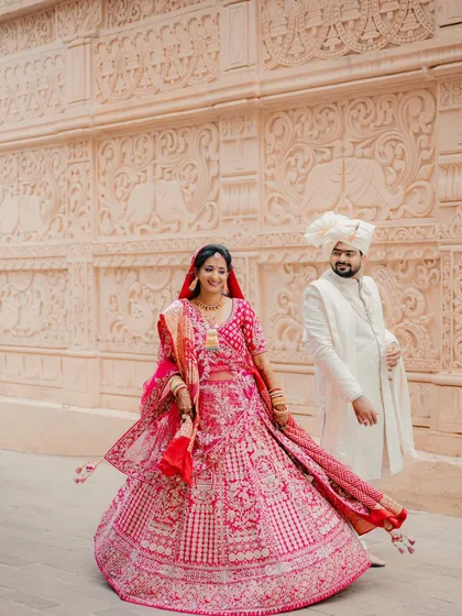 A dynamic shot of the couple walking, with the bride's lehenga in full twirl. This captures movement and joy against a beautifully carved wall.