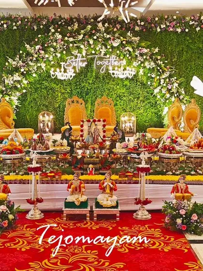A grand engagement setup with a green wall backdrop and golden chairs. The plate decoration is elaborate and fills the entire stage.