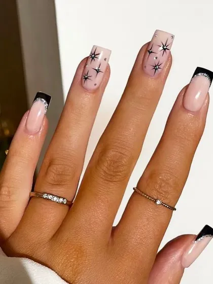 A glamorous take on celestial nails, with black starbursts on a sheer nude base and sparkling black glitter French tips.