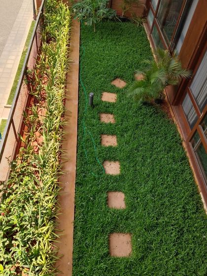 An overhead view of a long, narrow garden with a lush lawn, stepping stones, and a dense row of border plants.
