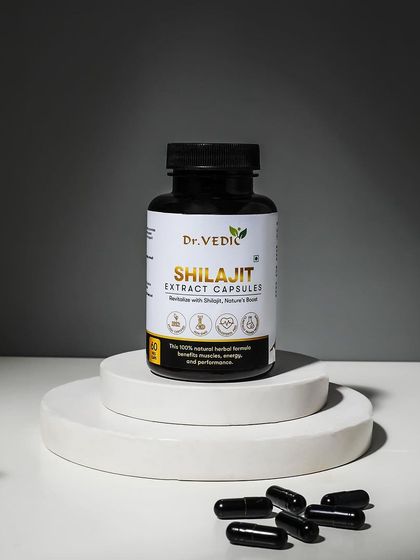 A powerful and simple shot of Shilajit extract capsules. The stark contrast of the black capsules on a white podium against a grey background creates a bold and modern look.