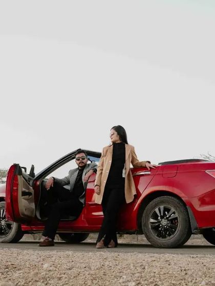 The couple poses with their red convertible, capturing a sense of adventure and modern style against the rustic landscape.