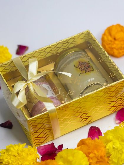 This golden gift box is perfect for any festive occasion. Here, it's filled with a scented candle and other skincare goodies, tied with a beautiful ribbon.