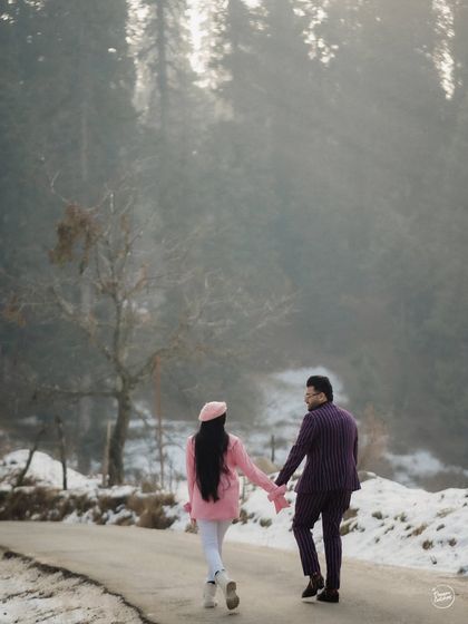 The journey begins. A couple walks hand-in-hand down a winding road in Kashmir, surrounded by snow and towering trees. This shot captures the sense of adventure and shared path that defines a pre-wedding elopement.