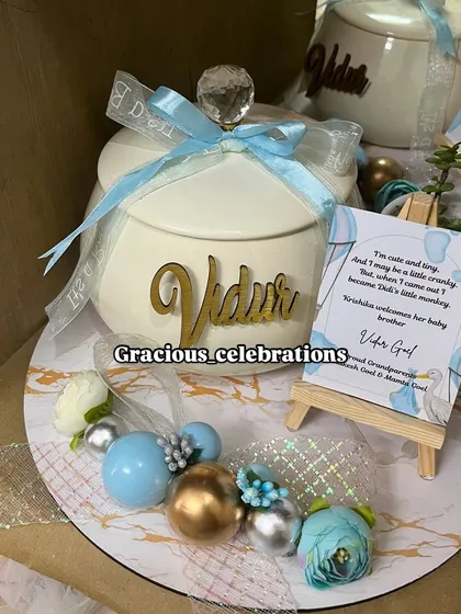 A close-up of our personalized baby announcement platter. This one features an elegant ivory handi for sweets like rasgulla or panjeeri, a live plant, and a custom card on a mini easel, all personalized with the baby's name.