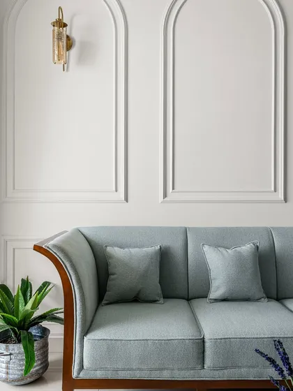 A detail shot focusing on the elegant curves of a light blue sofa set against a wall with classic arch moldings. The brass wall sconce adds a touch of warmth and sophistication, highlighting the room's refined details.
