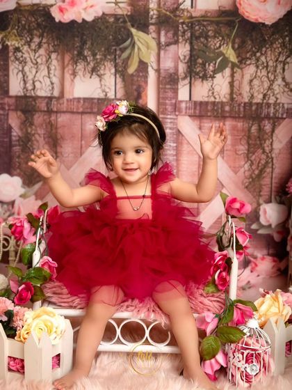 A full view of the beautiful floral setup for a first birthday, with the toddler girl sitting happily on a prop bed.