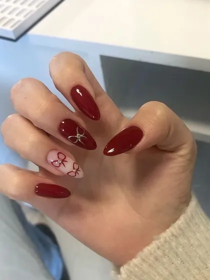Nail inspiration for a bolder coquette look with deep red polish and delicate bow art.