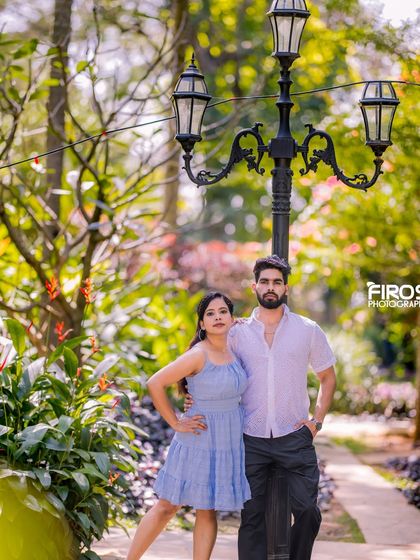 A stylish couple poses by a classic lamppost on a garden pathway, a simple yet elegant setting for a pre-wedding shoot.