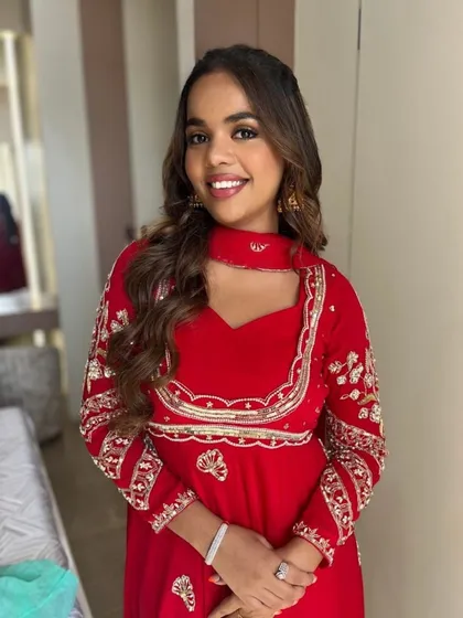 A bright, smiling portrait. The makeup is minimal and radiant, letting her natural beauty and the vibrant red of her outfit shine.
