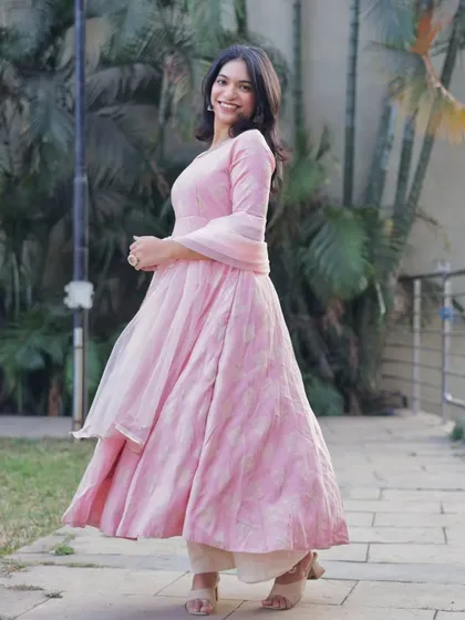 A joyful, full-length shot of a woman twirling in a flowing pink Anarkali, capturing the movement and happiness of the moment.