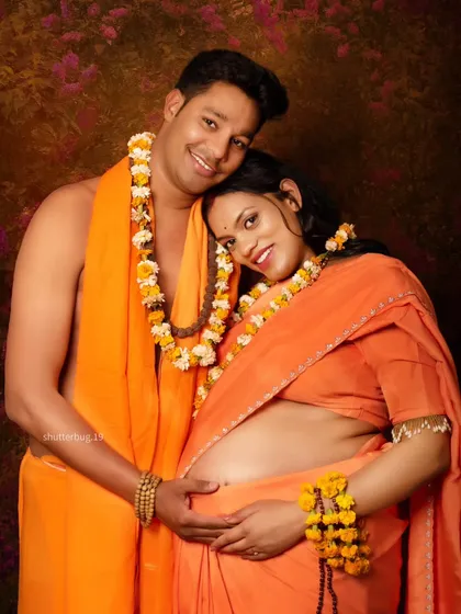 A warm and loving portrait of the couple from their Ram Sita themed shoot. They embrace gently, both dressed in traditional saffron-colored attire, smiling happily for the camera.