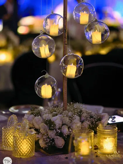 An elegant and intimate tablescape detail, with hanging glass globes holding candles that cast a magical glow over a centerpiece of baby's breath and white roses.