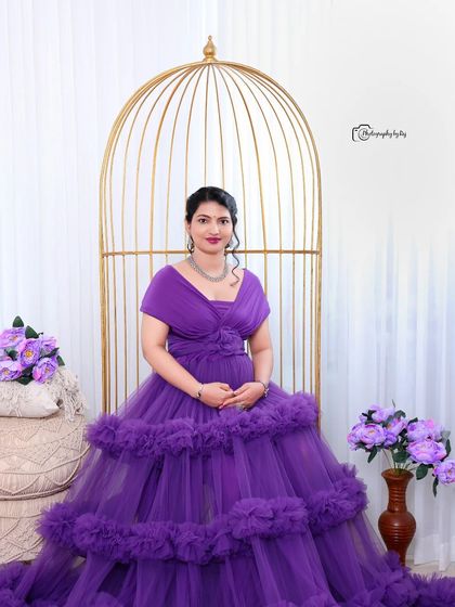 A beautiful studio portrait of a mother-to-be in a purple ruffled gown, seated in a golden birdcage chair.