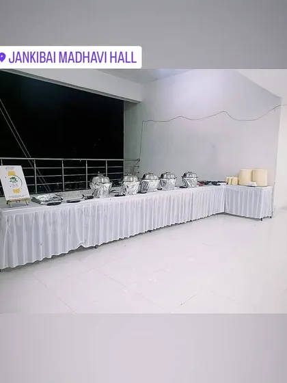 A long shot of a clean, white-themed buffet setup at Jankibai Madhavi Hall before an event.
