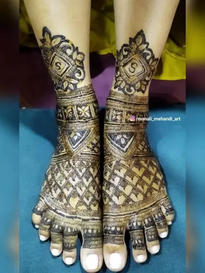 This foot design features the bride's initial 'S' inside a decorative frame on the ankle. The rest of the foot is covered in a dense, traditional jaal pattern.