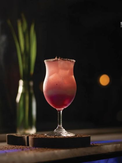 This layered cocktail with a sugared rim is one of my specialties. It's served on the rooftop, with the blurred city lights in the background creating a perfect evening ambiance.
