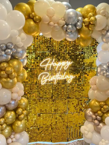 Classic glamour with a gold sequin wall. Framed by a white, gold, and silver balloon arch and a "Happy Birthday" neon sign, this is a timeless look for any celebration.