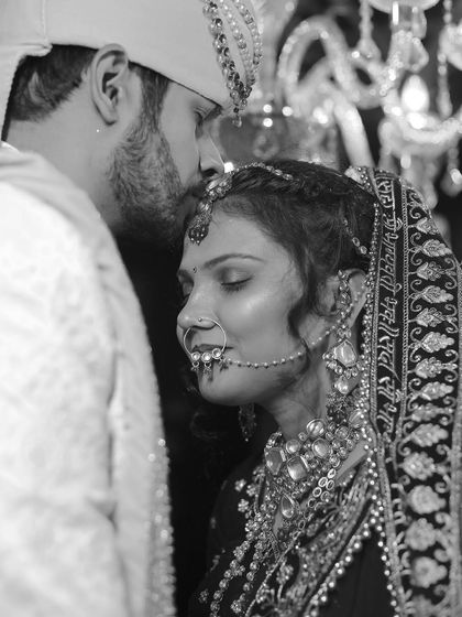 A powerful and emotional black and white close-up. The groom's tender kiss on the bride's forehead is a timeless expression of love and protection, captured beautifully.